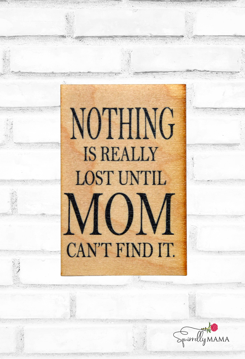 Wooden magnet with humorous quote 'Nothing is really lost until Mom can't find it.' on a white brick wall background.