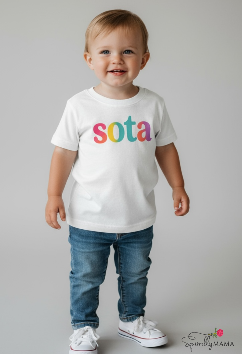 Child wearing a white t-shirt with 'sota' in colorful letters on a plain background