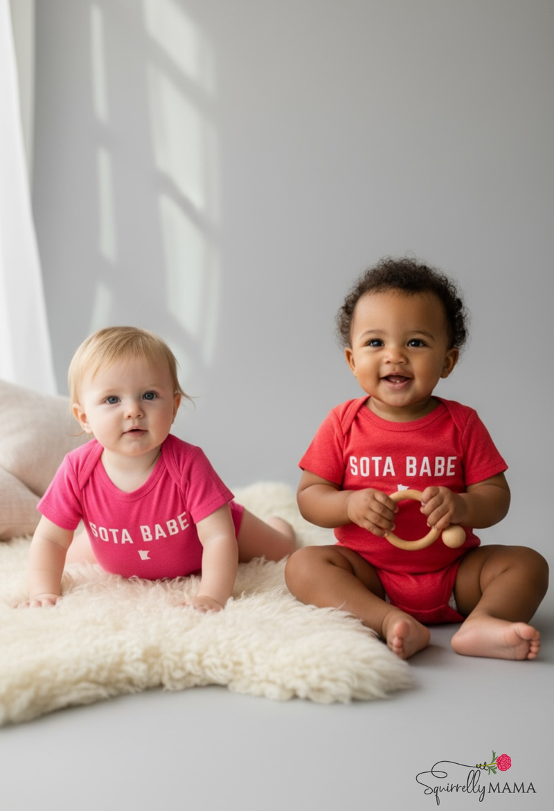 Two children wearing 'SOTA BABE' shirts sitting on a white surface with a gray background.