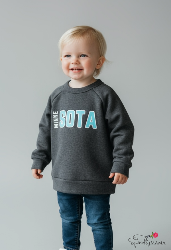 Child wearing a gray sweatshirt with 'MINNESOTA' printed on it against a plain background