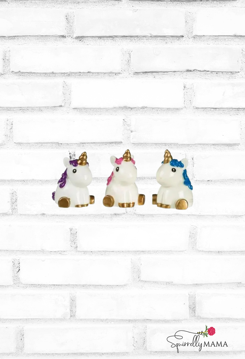 three little unicorn lipsticks one blue one pink one purple on brick background with squirrelly mama logo in corner