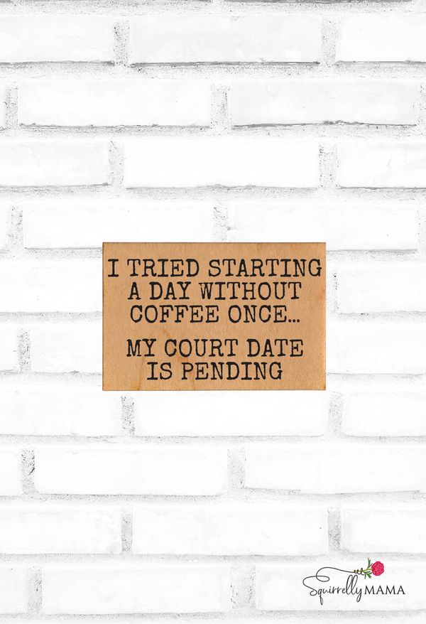 Wooden magnet with humorous coffee-themed text on a white brick wall background