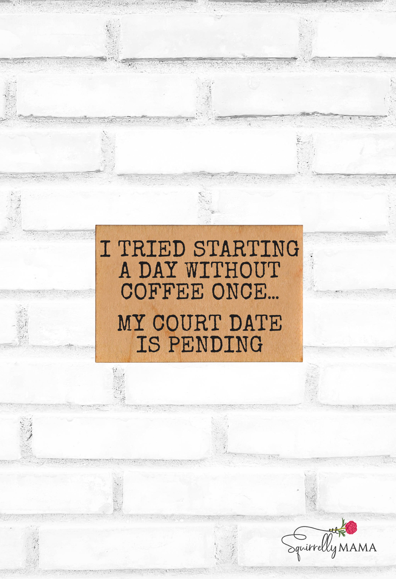 Wooden magnet with humorous coffee-themed text on a white brick wall background