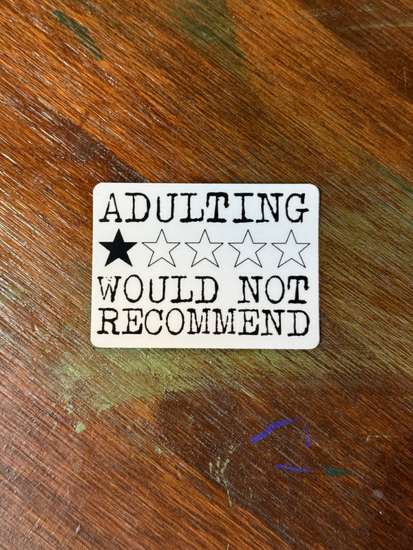 Sticker with 'ADULTING would not recommend' text on a wooden surface