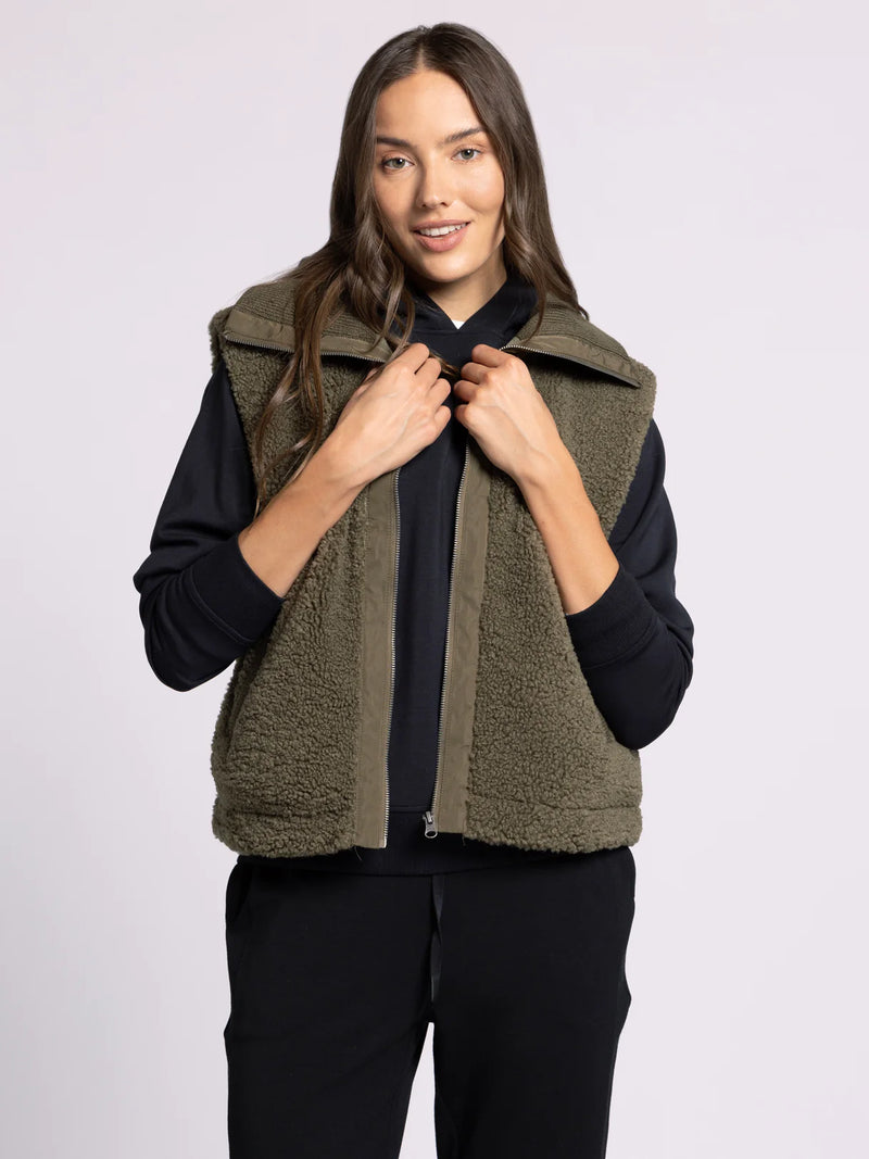 Woman wearing a green vest over a black shirt on a white background