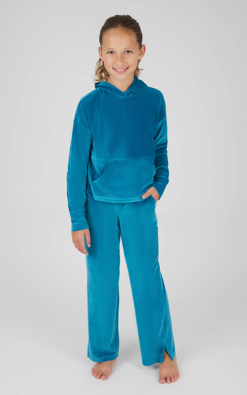 A girl standing and posing in a blue velour hoodie and straight pants set with rib detailing and a drawcord waistband.