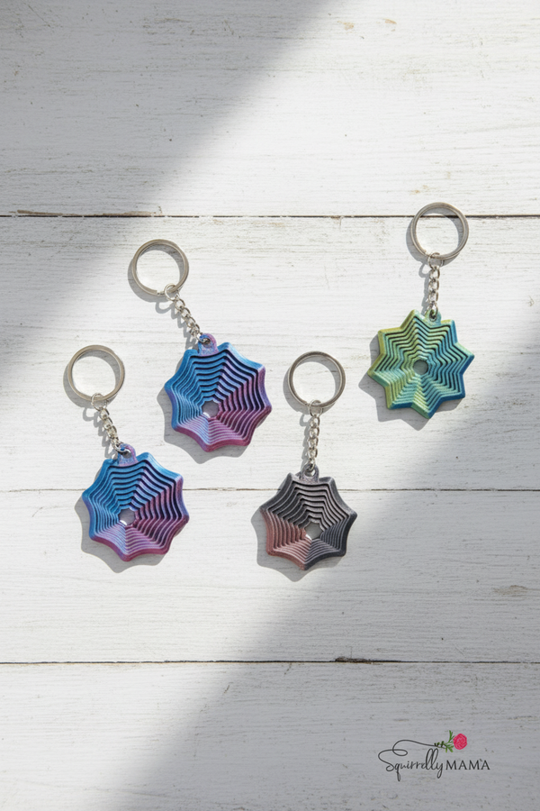 Four spider web fidhet keychains in different colors on a white background