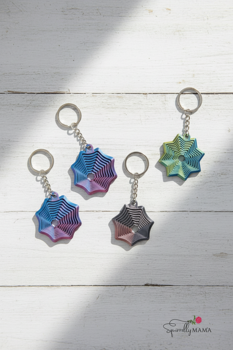 Four spider web fidhet keychains in different colors on a white background