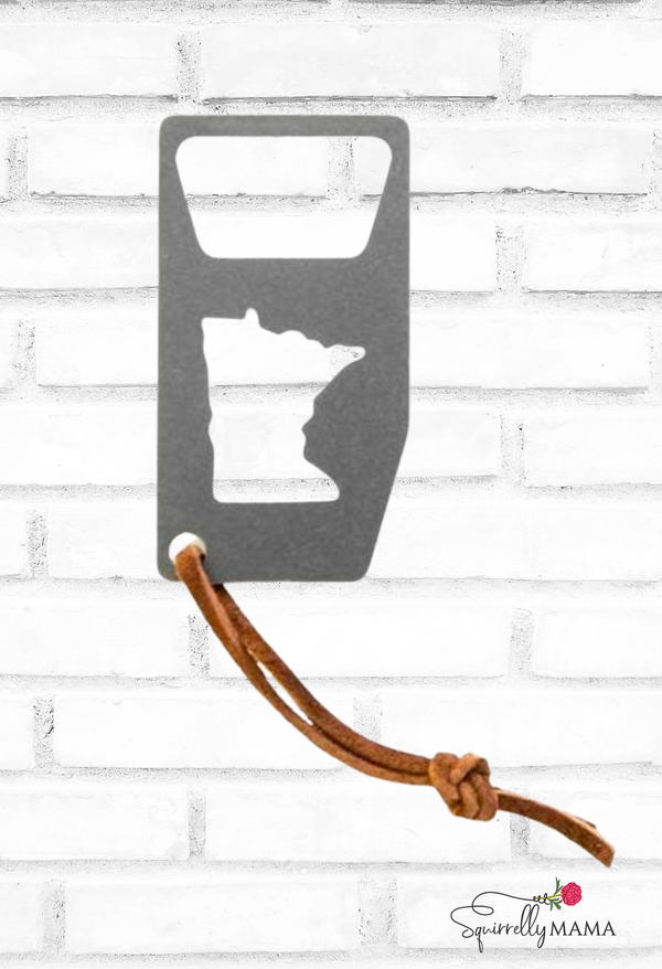 Metal bottle opener shaped like the state of Minnesota with a leather strap on a white brick background.